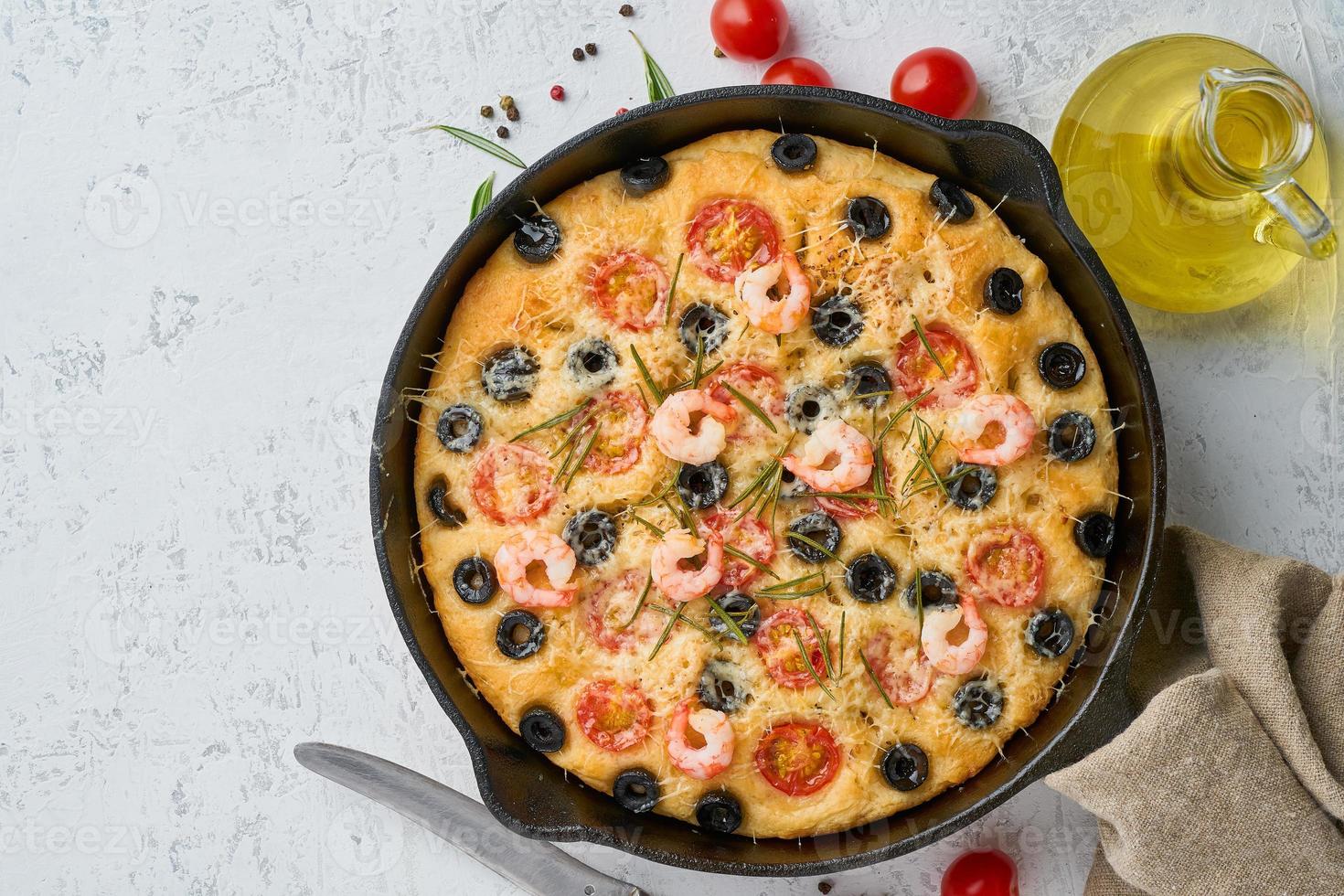 Focaccia, shrimp pizza in skillet, italian flat bread with tomatoes, olives and rosemary. Top view, copy space, white concrete background photo