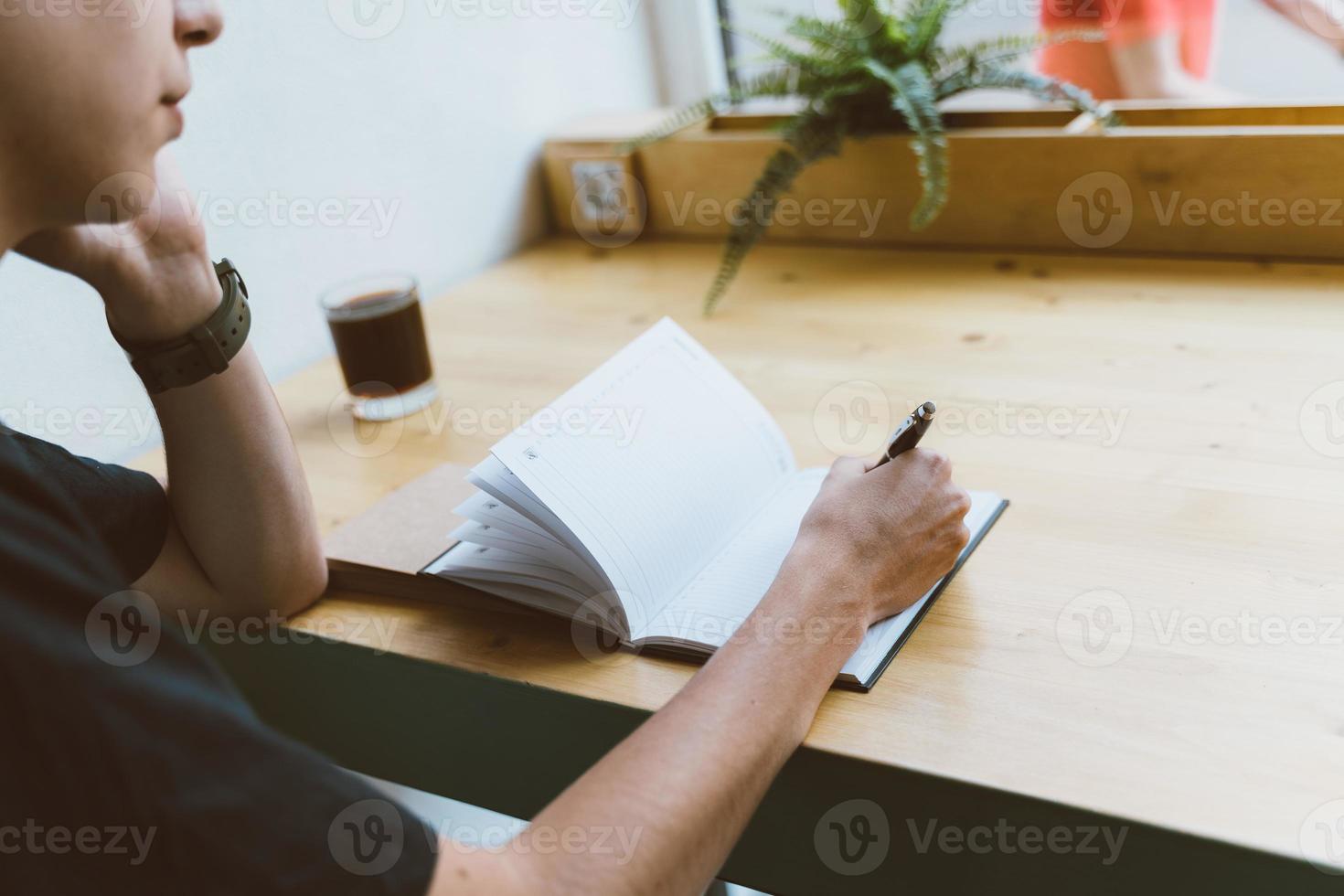 Young man writing information to notepad and speaking mobile phone, teenager in casual clothes plans a schedule photo