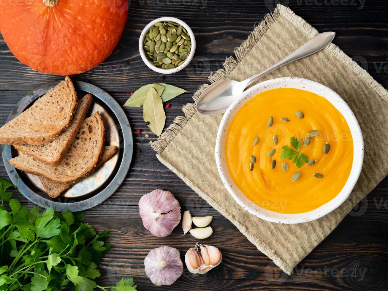 sopa de calabaza triturada en un plato blanco, semillas de calabaza, pan, ajo sobre fondo de madera oscura foto