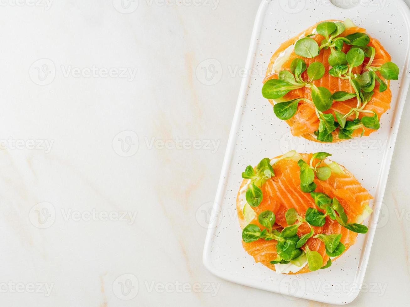 dos sándwiches con salmón, queso crema, rodajas de pepino sobre una mesa de mármol blanco foto