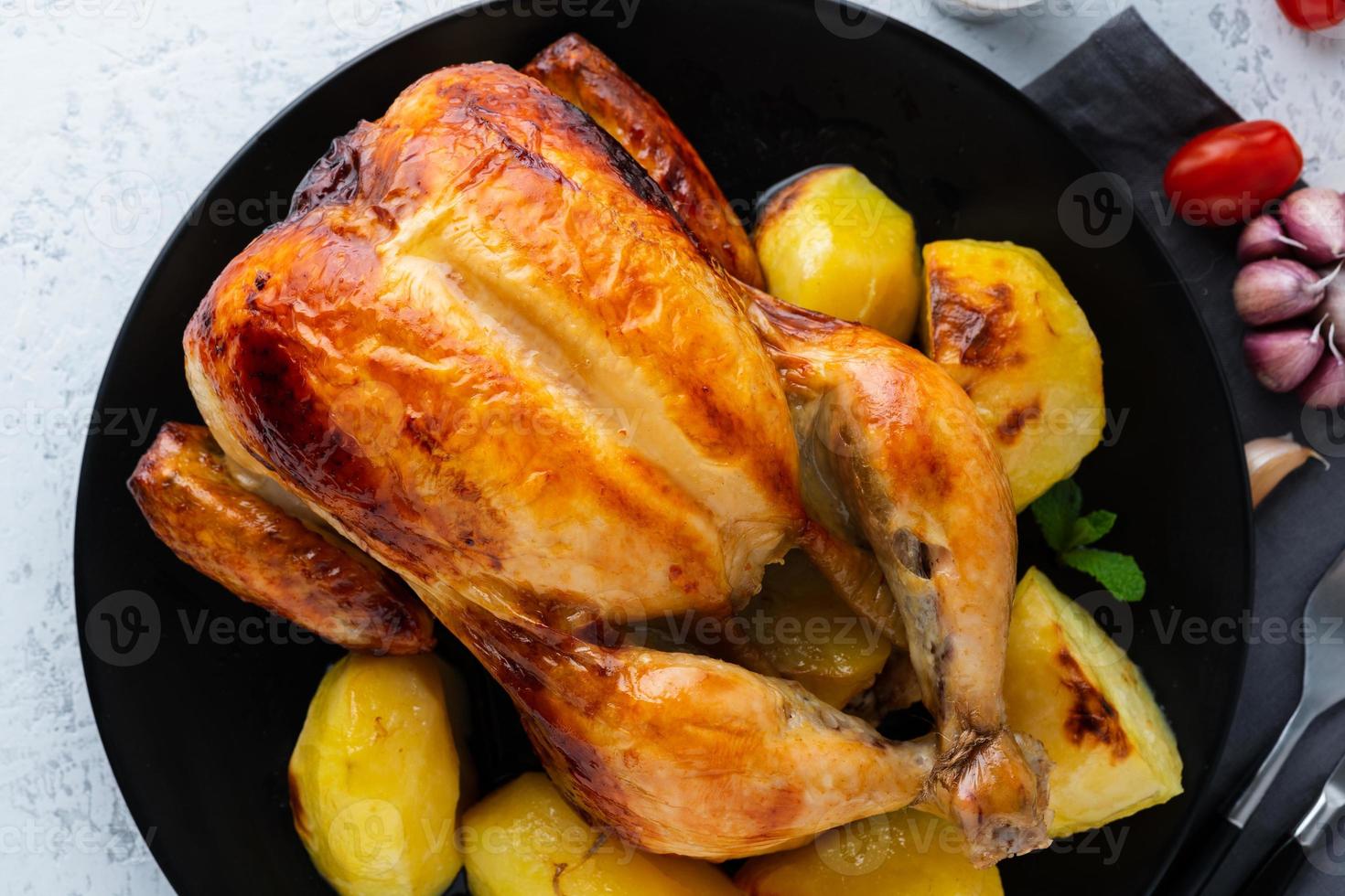 Grilled whole chicken in black plate on white table, baked meat with potatoes. Top view, close up photo