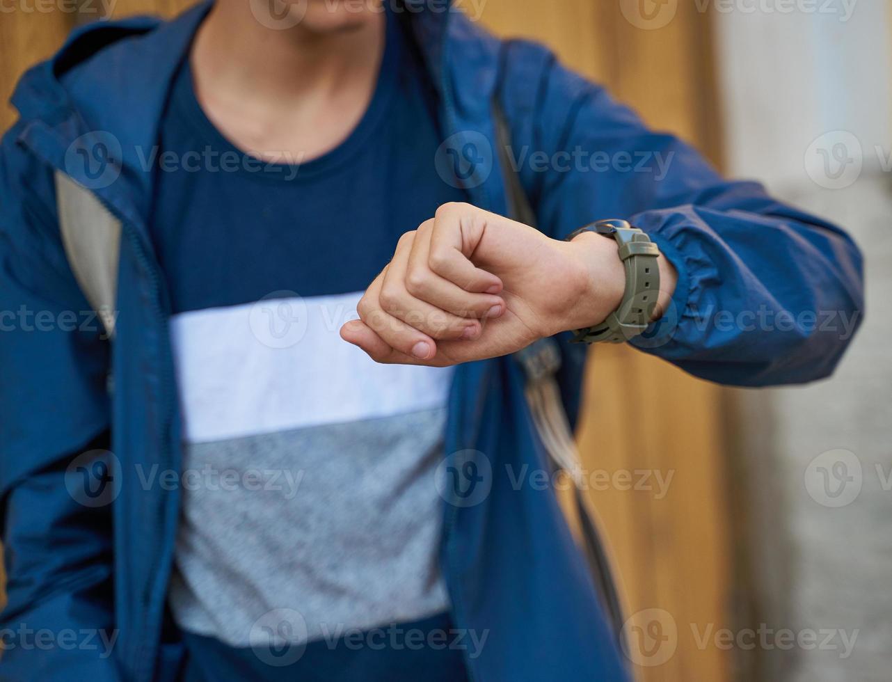 Young adult looks at the clock, waiting for a meeting with friends. A man is waiting for a woman in a street of city on a date, looking at watch photo