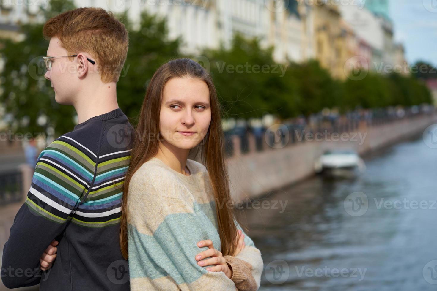 retrato de una pareja feliz, de pie espalda con espalda en el centro de la ciudad, hombre pelirrojo con anteojos, mujer hermosa con cabello largo y oscuro foto