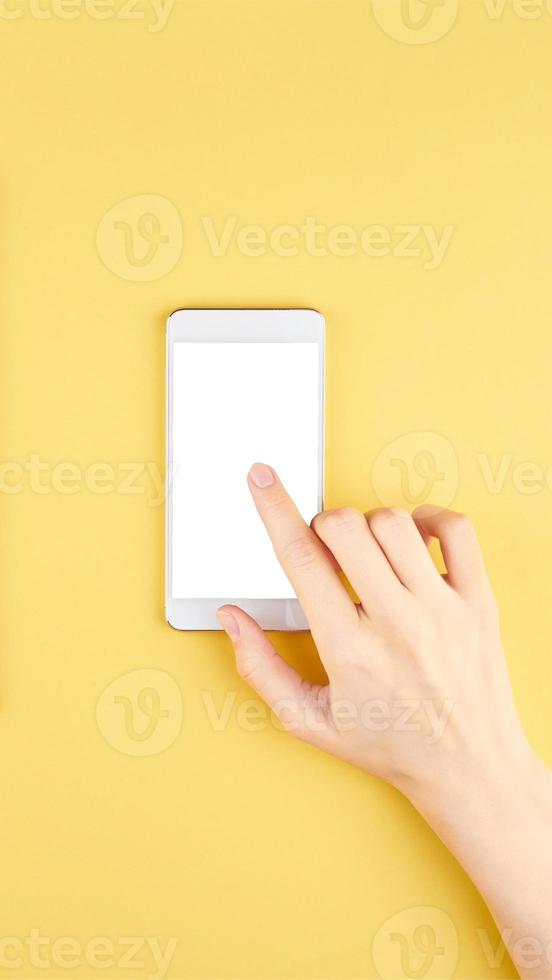 Female hand holding a modern gadget and pointing with finger, top view, on yellow background photo