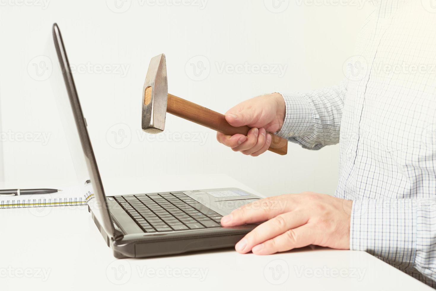 The man raised a hammer over the computer, man in the shirt wants to break the laptop. The concept of fatigue from work photo