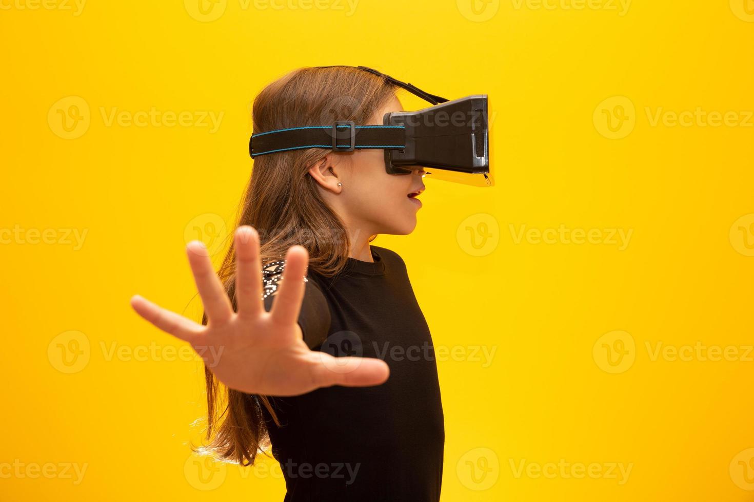 Happy little girl wearing virtual reality goggles watching movies or  playing video games. Cheerful smiling teenager looking in VR glasses. Funny  child experiencing 3D gadget technology - close up. 7547794 Stock Photo