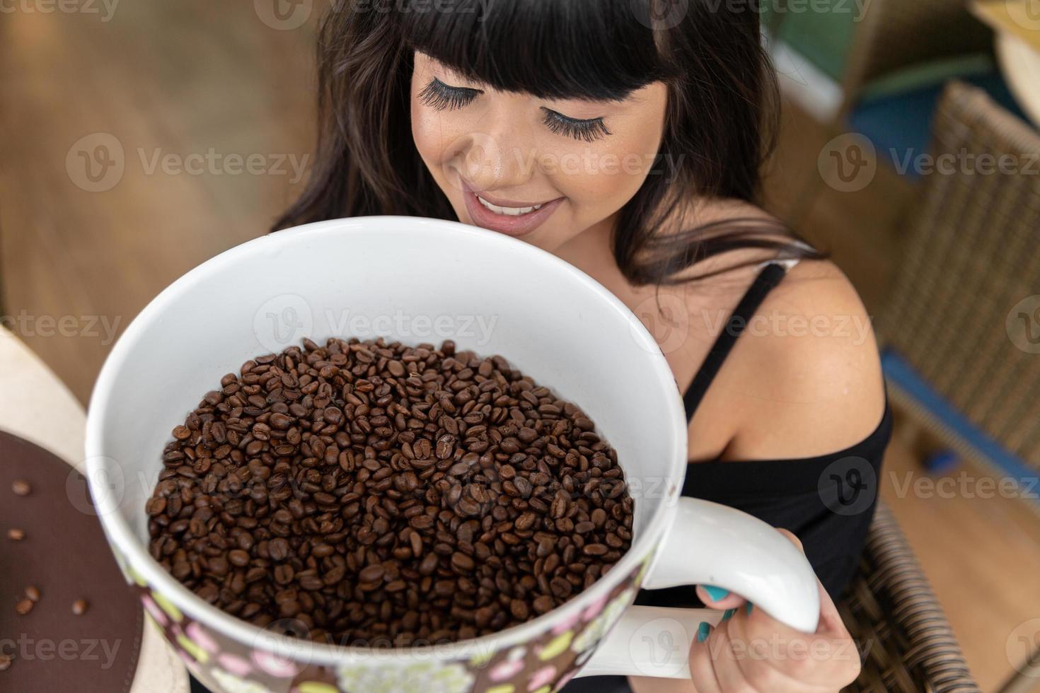 Beautiful brunette girl with a big ceramic mug with coffee seeds. Heap of coffee beans in cup. photo