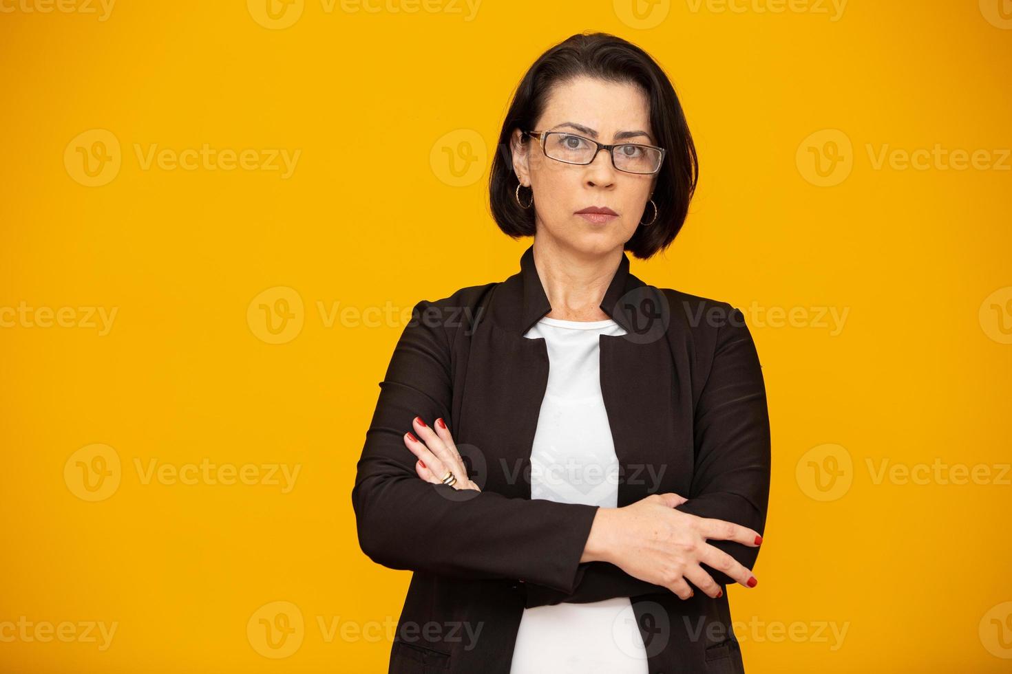 Attractive middle aged woman with beautiful smile on yellow wall. Pretty older business woman, successful confidence with arms crossed. photo