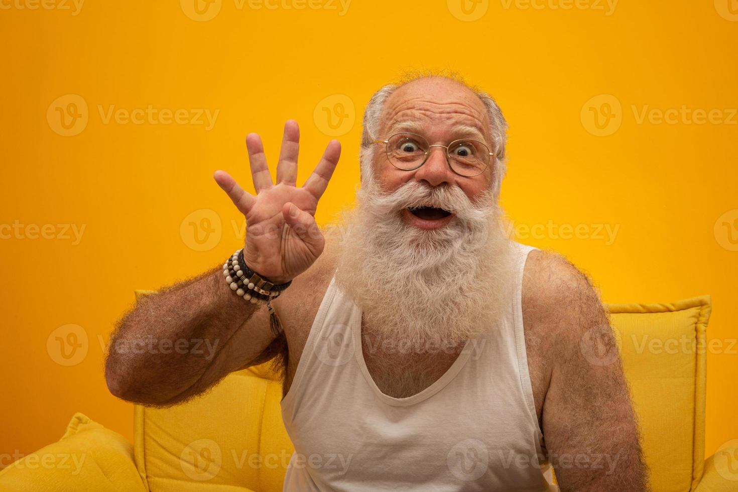 Smiling senior with a long white beard man making four times sign gesture with hand fingers on yellow background. Positive emotion facial expression feelings, attitude, symbol, countdown. photo