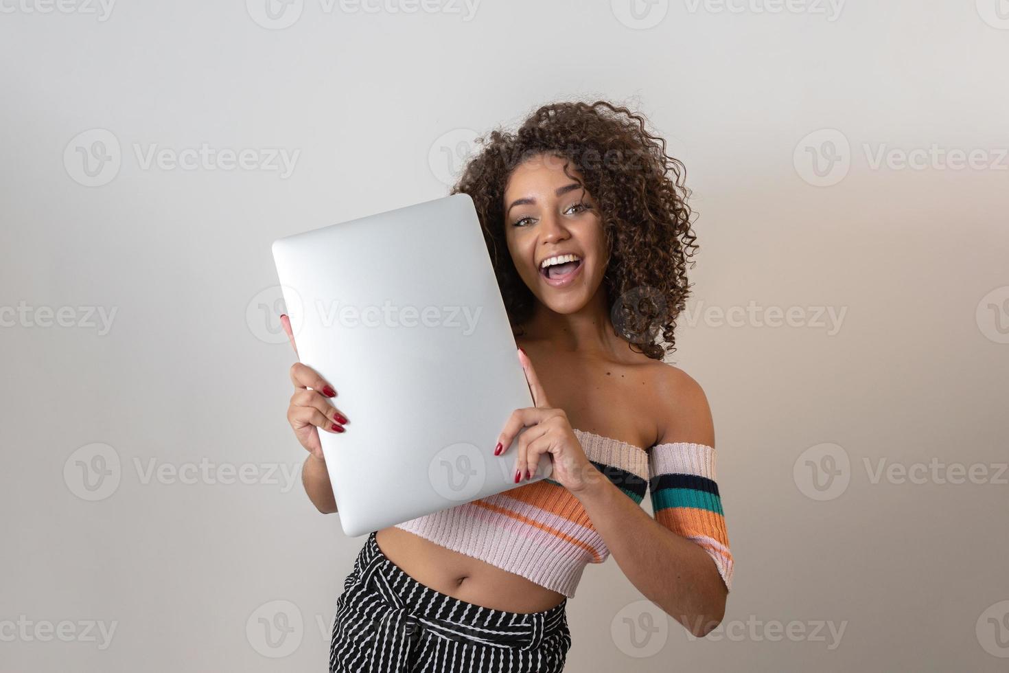 Portrait of smiling young afro american woman holding laptop computer over white background photo