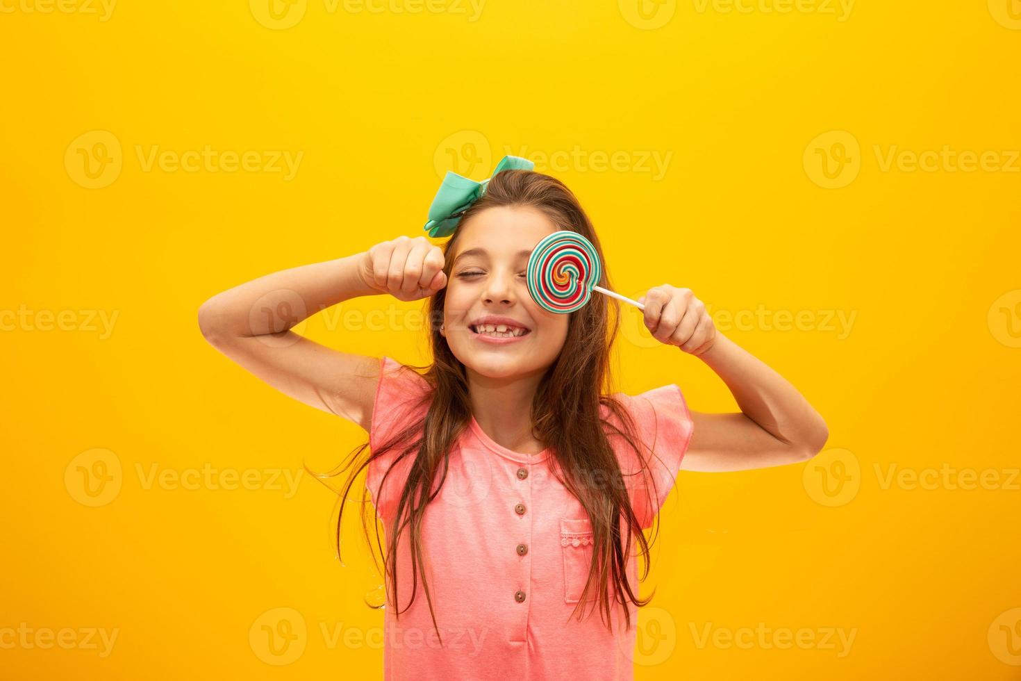 The child is holding a lollipop. Childish joy is sweetness. Little girl on yellow background. photo