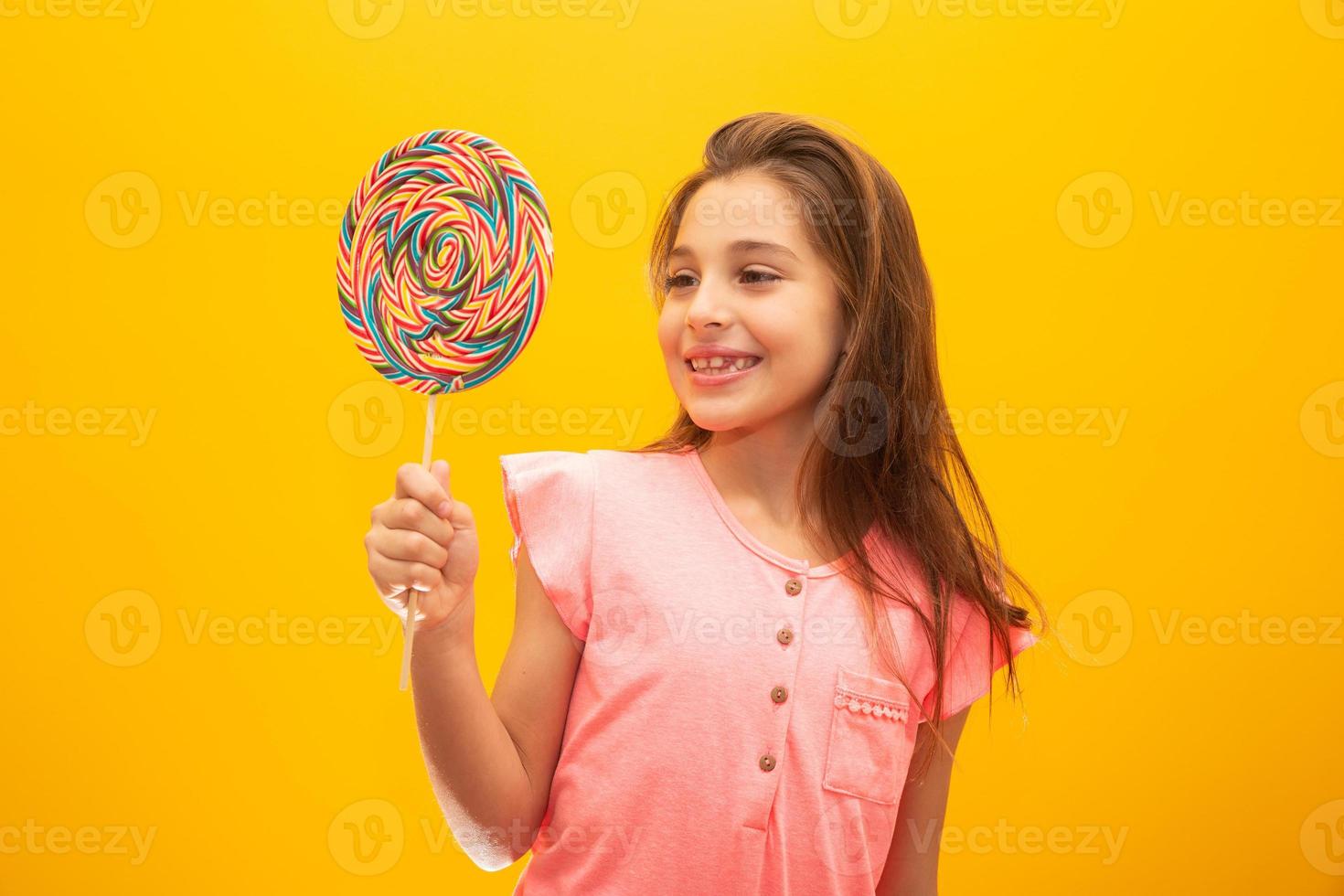 The child is holding a lollipop. Childish joy is sweetness. Little girl on yellow background. photo