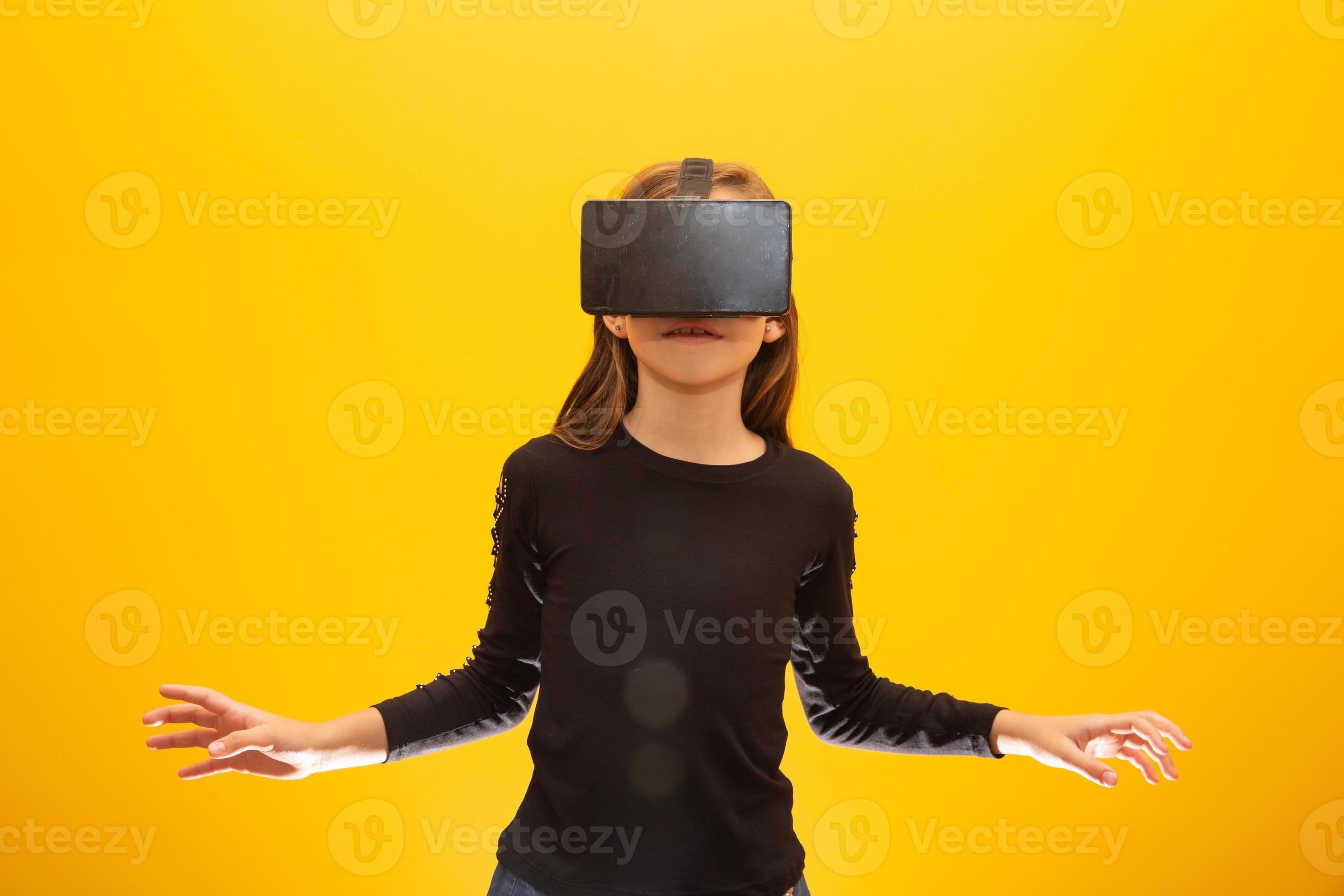 Happy little girl wearing virtual reality goggles watching movies or  playing video games. Cheerful smiling teenager looking in VR glasses. Funny  child experiencing 3D gadget technology - close up. 7548181 Stock Photo