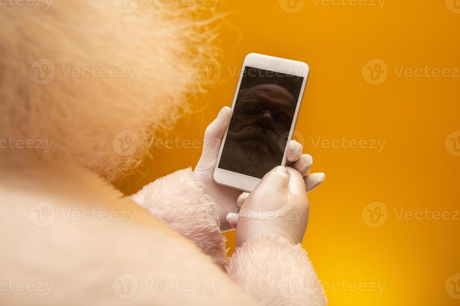 Santa Claus working using smartphone on yellow texture background surface. Close up top view on hands. Happy New Year and Merry Christmas photo