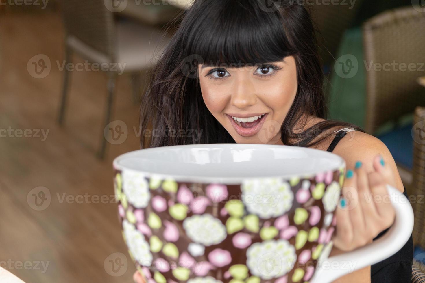 Beautiful brunette girl with a big ceramic mug with coffee seeds. Heap of coffee beans in cup. photo