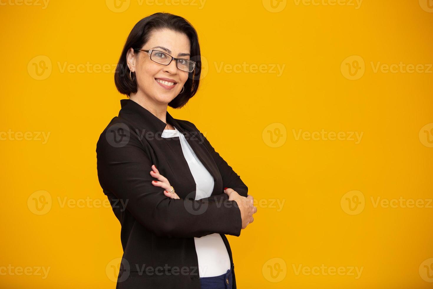 atractiva mujer de mediana edad con una hermosa sonrisa en la pared amarilla. mujer de negocios bastante mayor, confianza exitosa con los brazos cruzados. foto