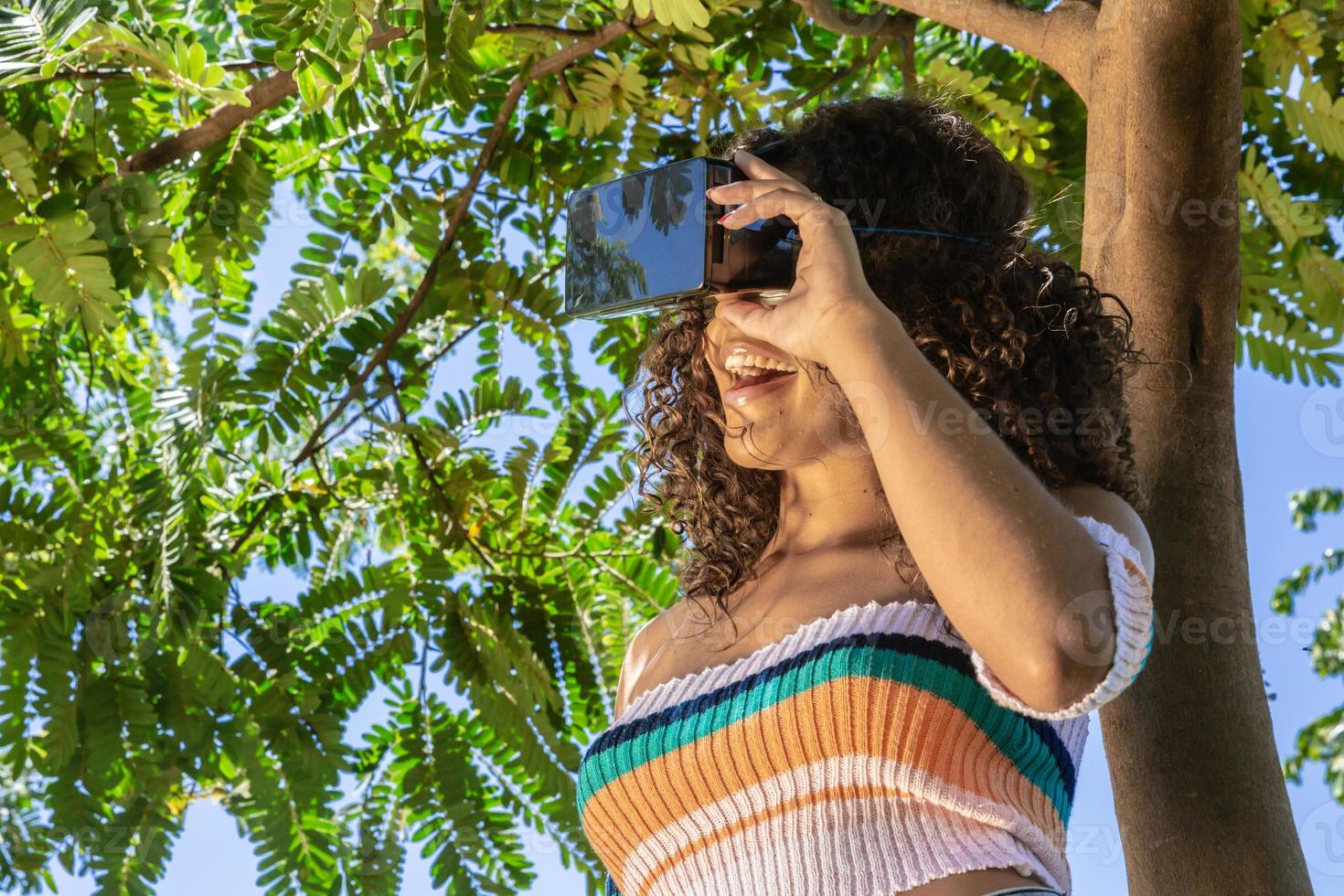 A beautiful young girl plays a game wearing virtual reality glasses on the park. VR headset photo