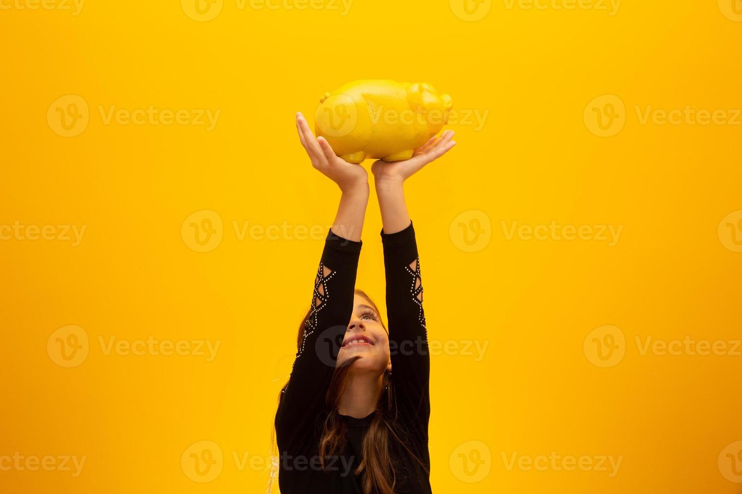 niña caucásica sobre fondo amarillo aislado sosteniendo una gran alcancía. foto