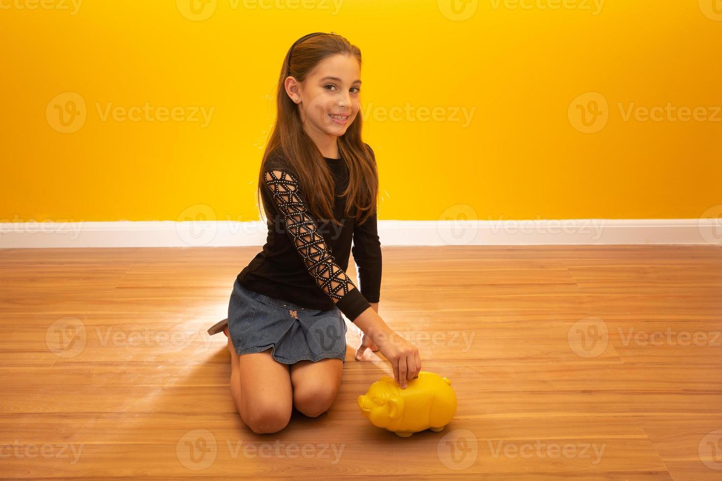 Caucasian little girl over yellow background holding a big piggybank. photo