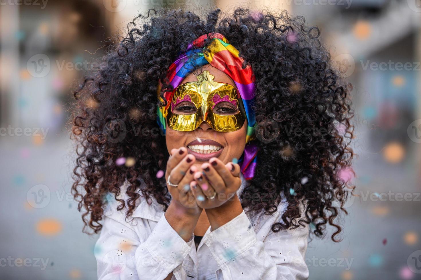 Carnaval party. Brazilian curly hair woman in costume blowing confetti photo