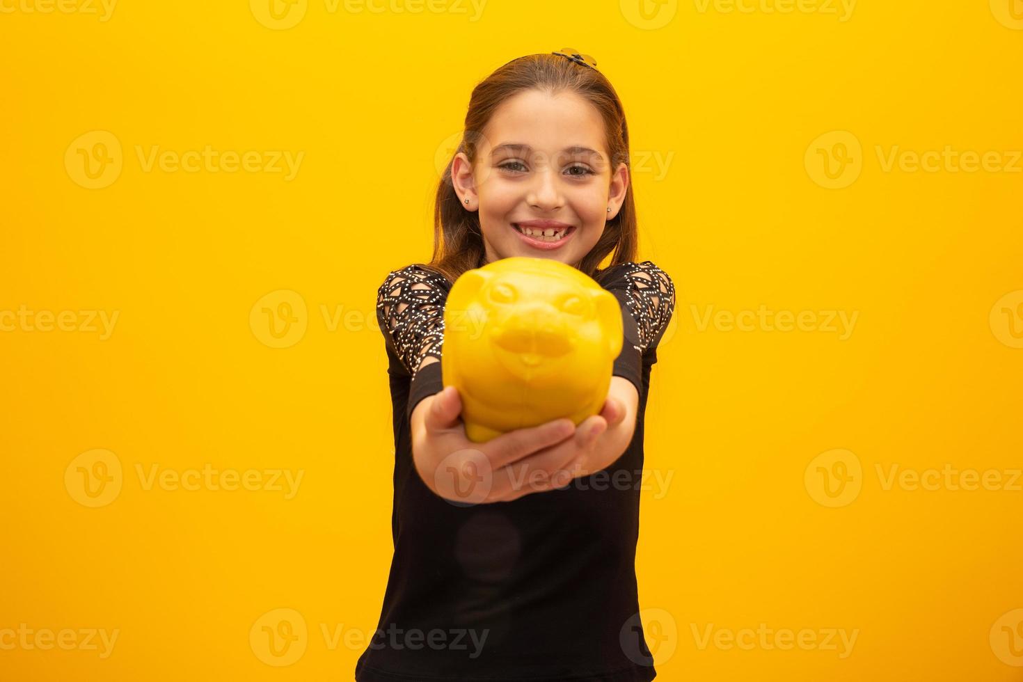 Caucasian little girl over isolated yellow background holding a big piggybank. photo