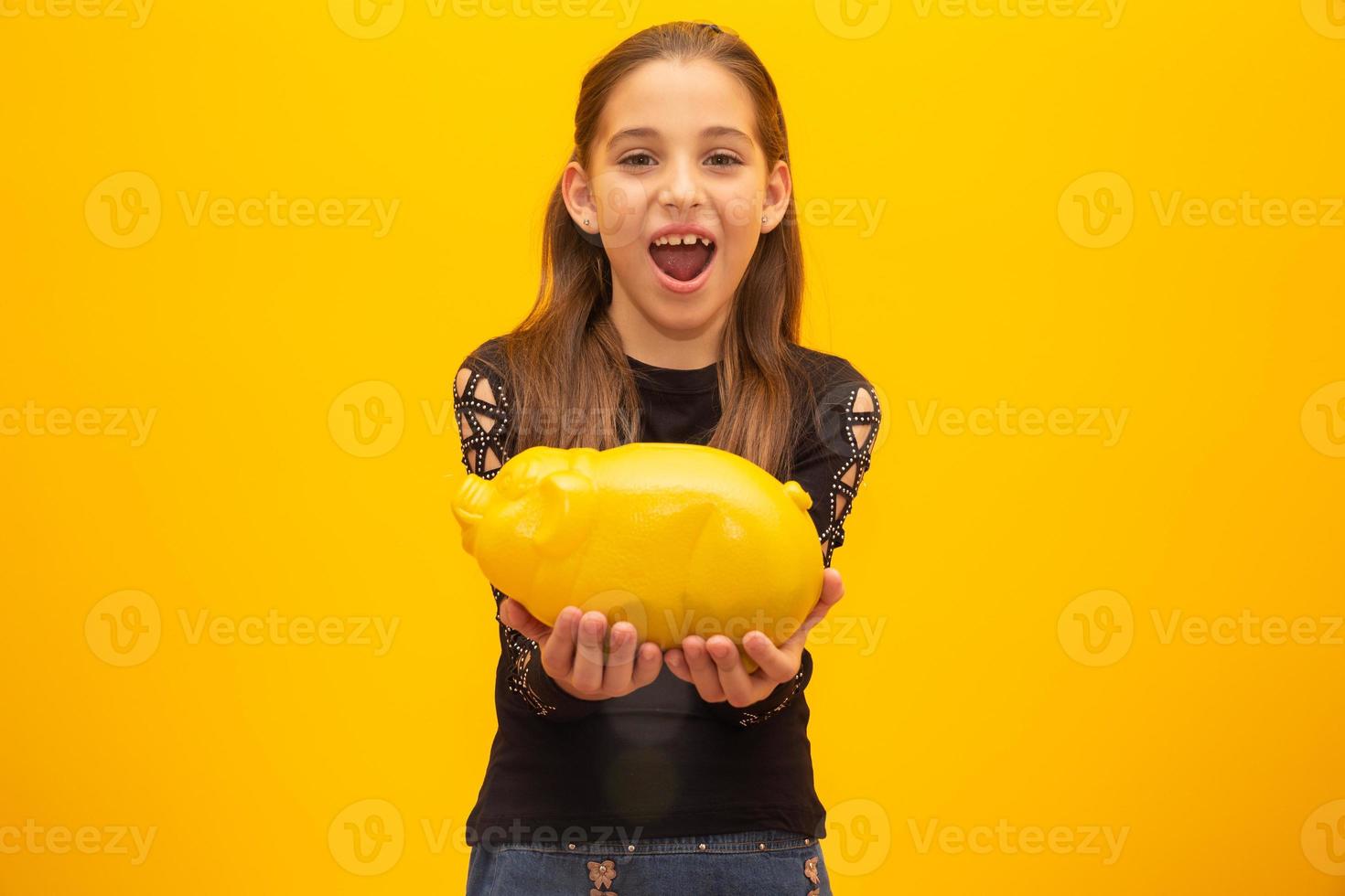 Caucasian little girl over isolated yellow background holding a big piggybank. photo