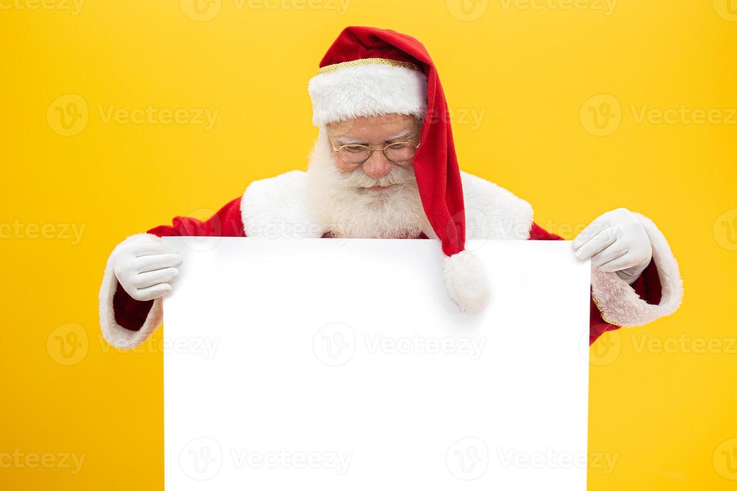 Happy Santa Claus looking out from behind the blank sign isolated on yellow background with copy space photo