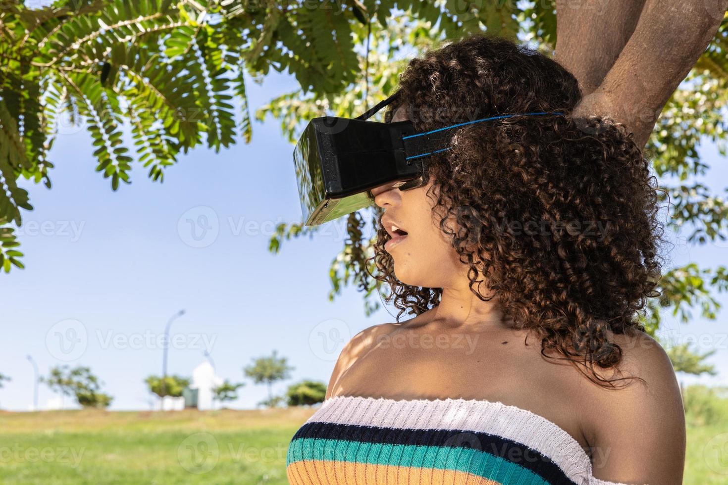 A beautiful young girl plays a game wearing virtual reality glasses on the park. VR headset photo