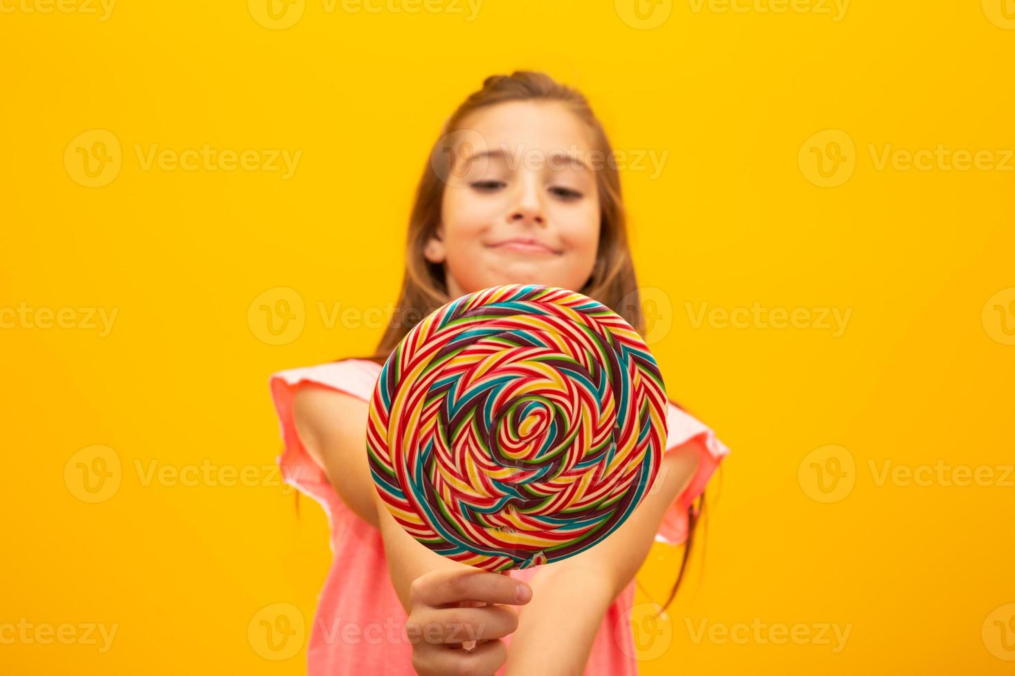 The child is holding a lollipop. Childish joy is sweetness. Little girl on yellow background. photo