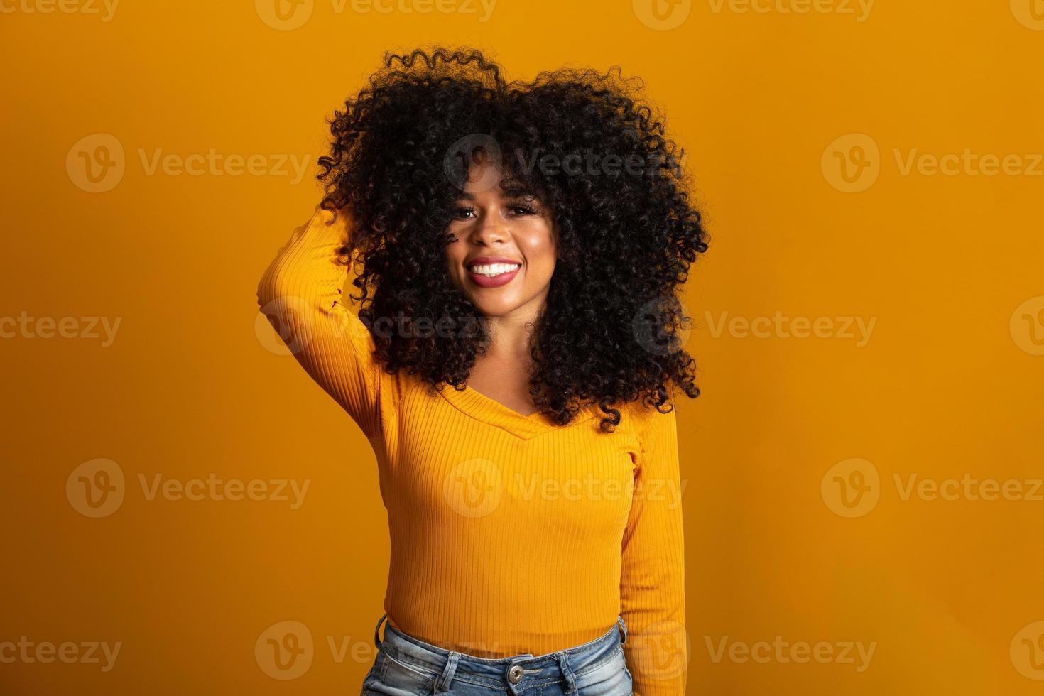 joven mujer afroamericana con cabello rizado mirando a la cámara y sonriendo. linda chica afro con cabello rizado sonriendo mirando a la cámara. foto