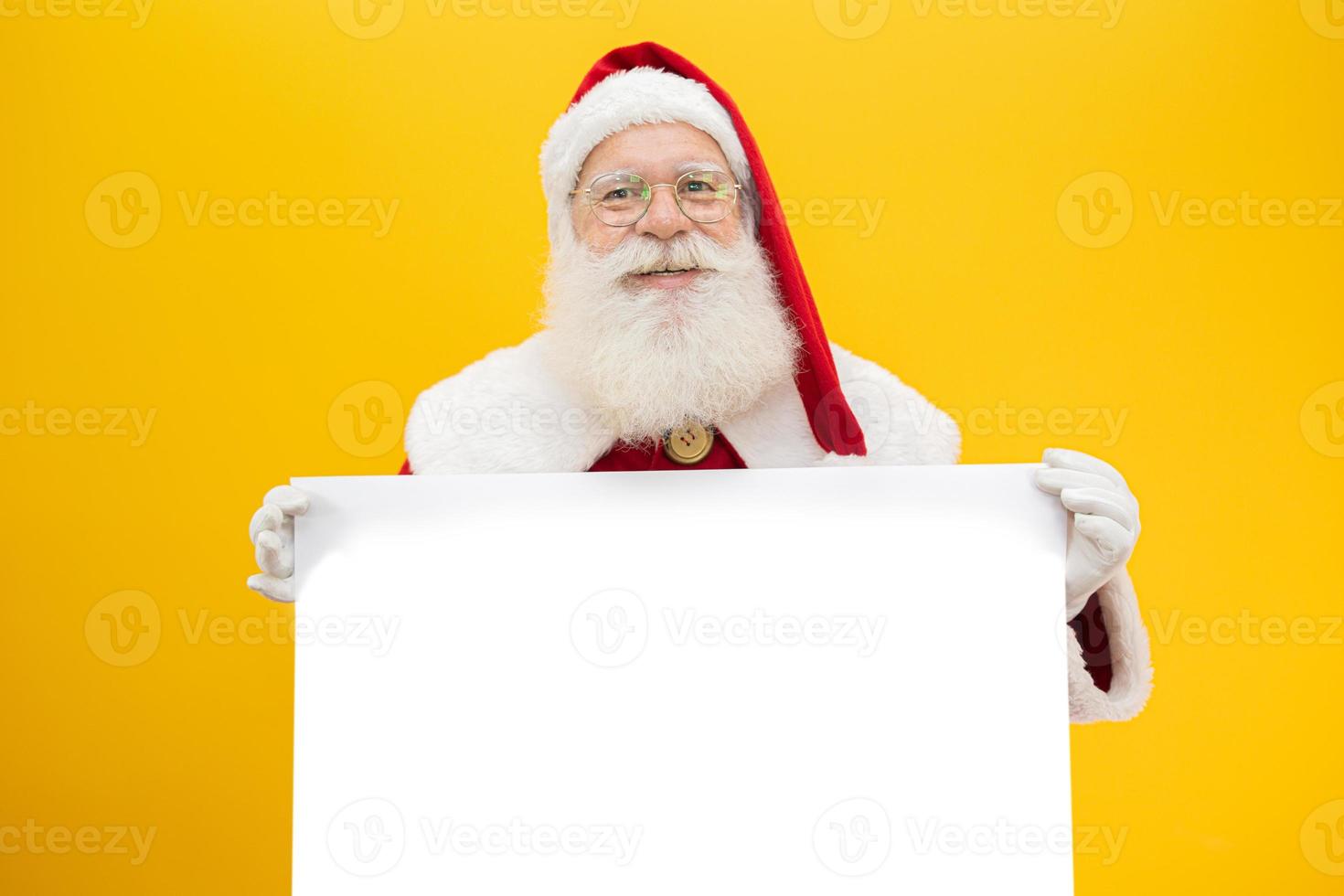 Happy Santa Claus looking out from behind the blank sign isolated on yellow background with copy space photo