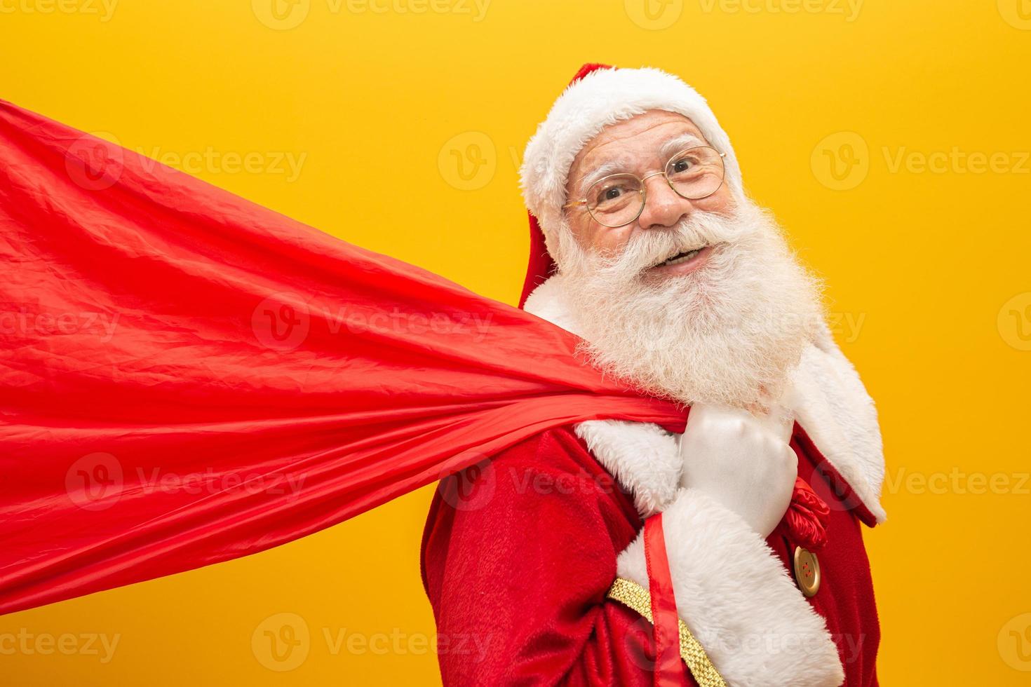 Santa Claus pulling huge bag of gifts on yellow background with copy space. Banner art. photo