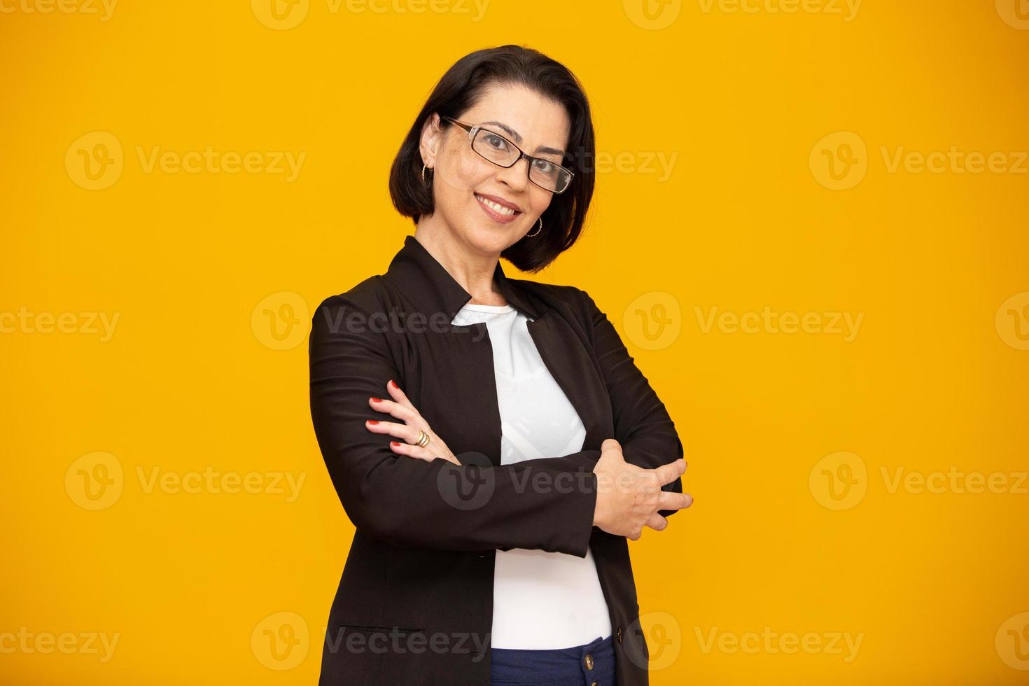 Attractive middle aged woman with beautiful smile on yellow wall. Pretty older business woman, successful confidence with arms crossed. photo