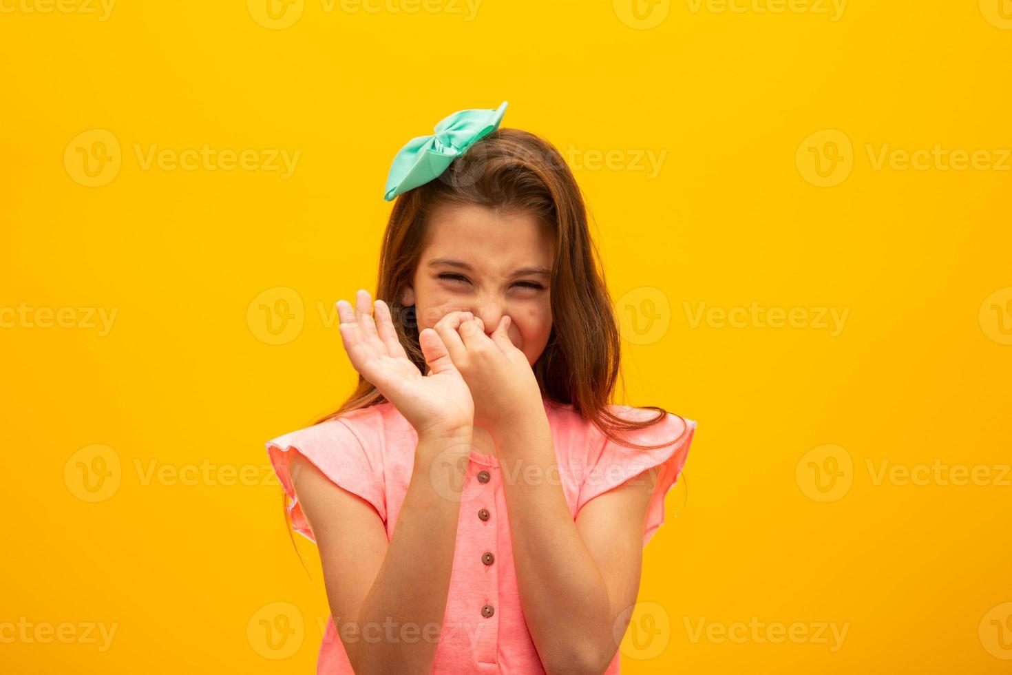 Young beautiful girl over isolated yellow background smelling something stinky and disgusting, intolerable smell, holding breath with fingers on nose. Bad smells concept. photo