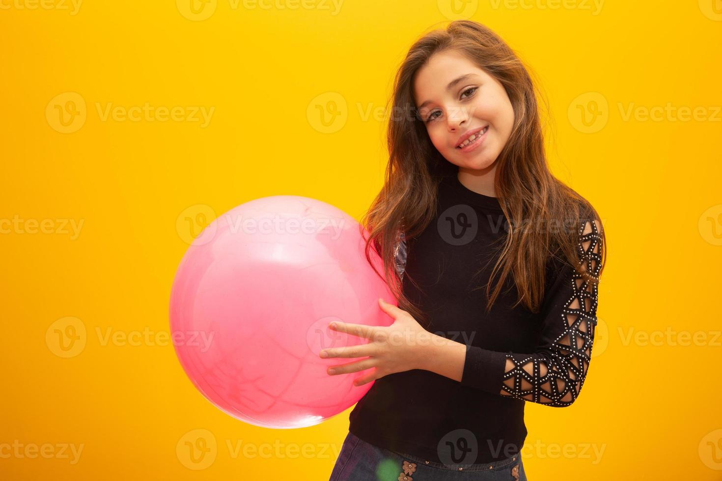 Beautiful young girl holding a pink ball on yellow background. photo