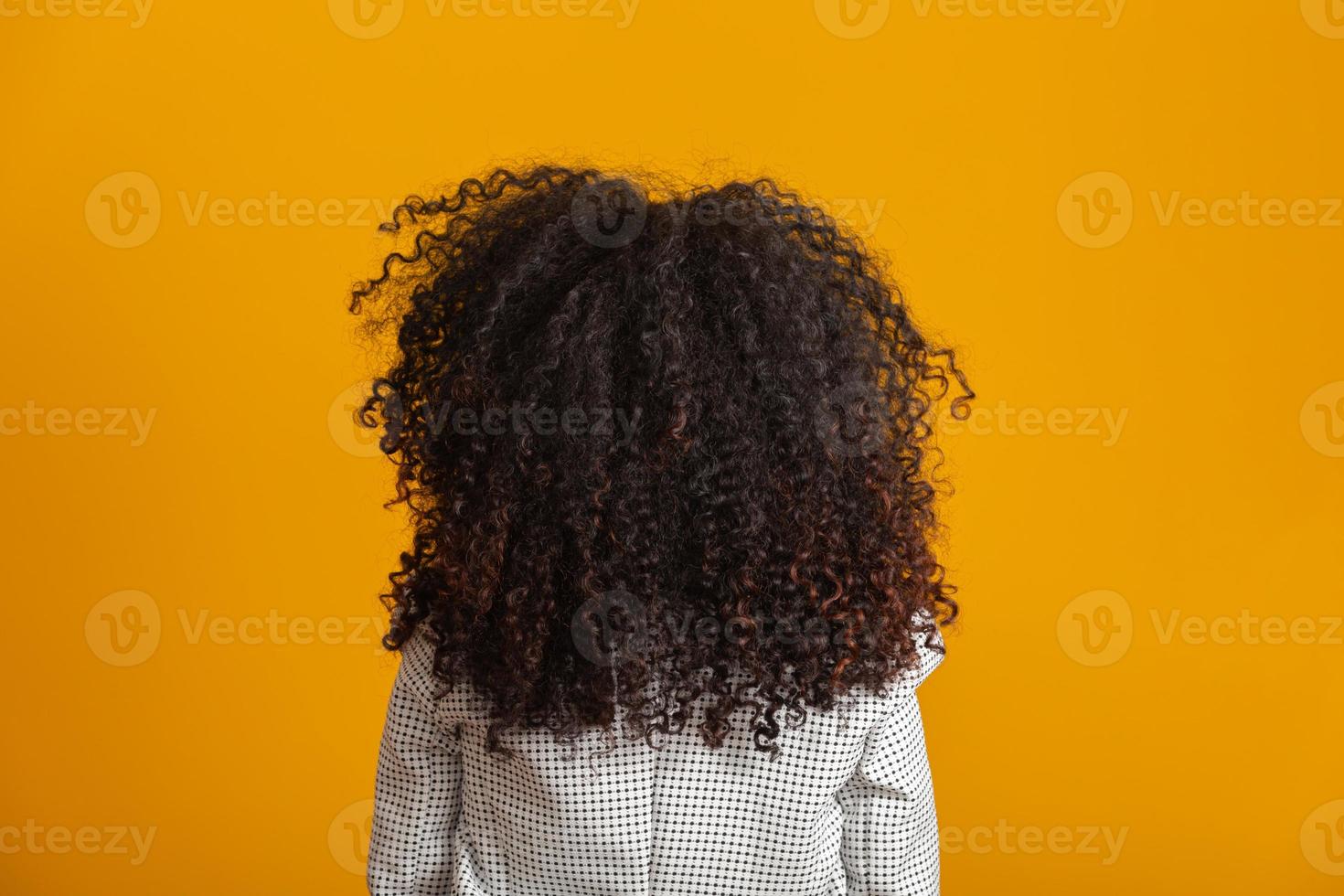 Young black woman on her back with afro hairstyle on yellow background. Girl with african hairstyle. Studio shot. photo