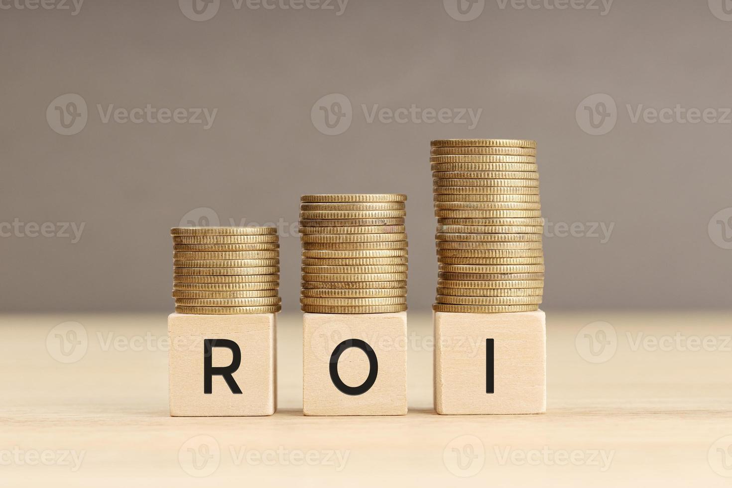 ROI word in wooden blocks with coins stacked in increasing stacks. Return on investment concept. Copy space photo