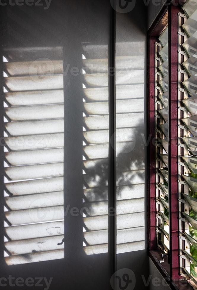 vista de primer plano de sombras de hojas espeluznantes con luces que brillan a través de una ventana con persianas de vidrio. Foto de stock en Vecteezy