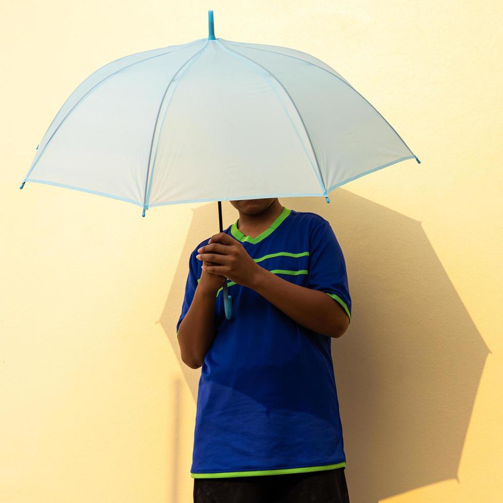 Close-up view of a young Thai boy wearing a blue t-shirt holding a blue umbrella. photo