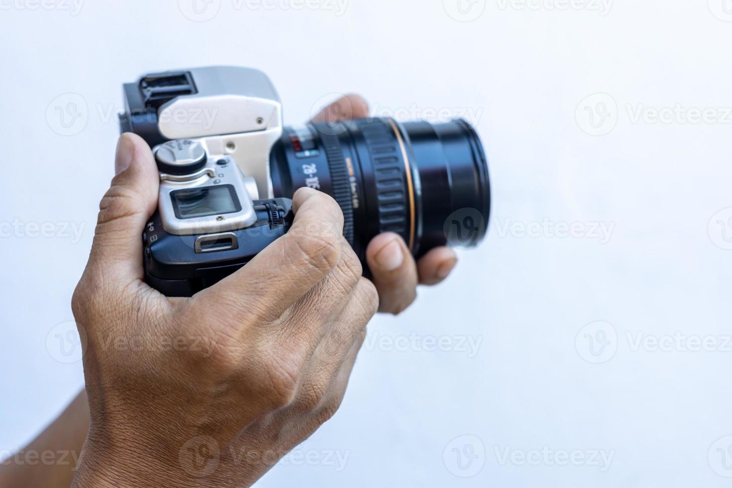 Isolated close-up of the hands and fingers of a Thai man holding an old black DSLR film camera. photo