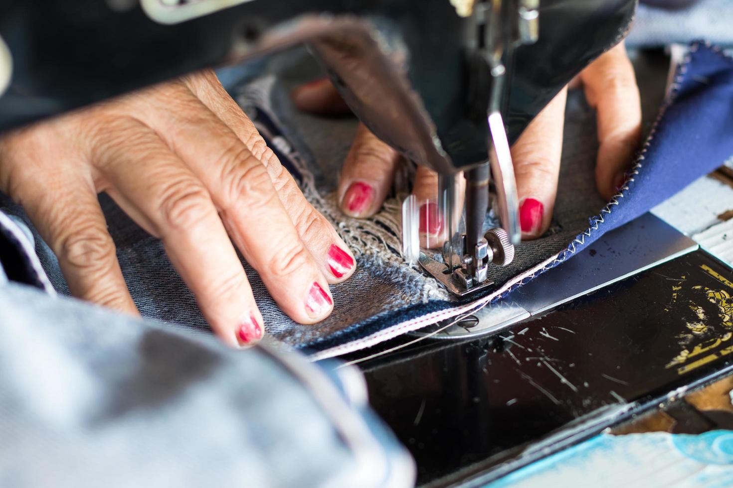 Red nail hand sewing jeans repair. photo