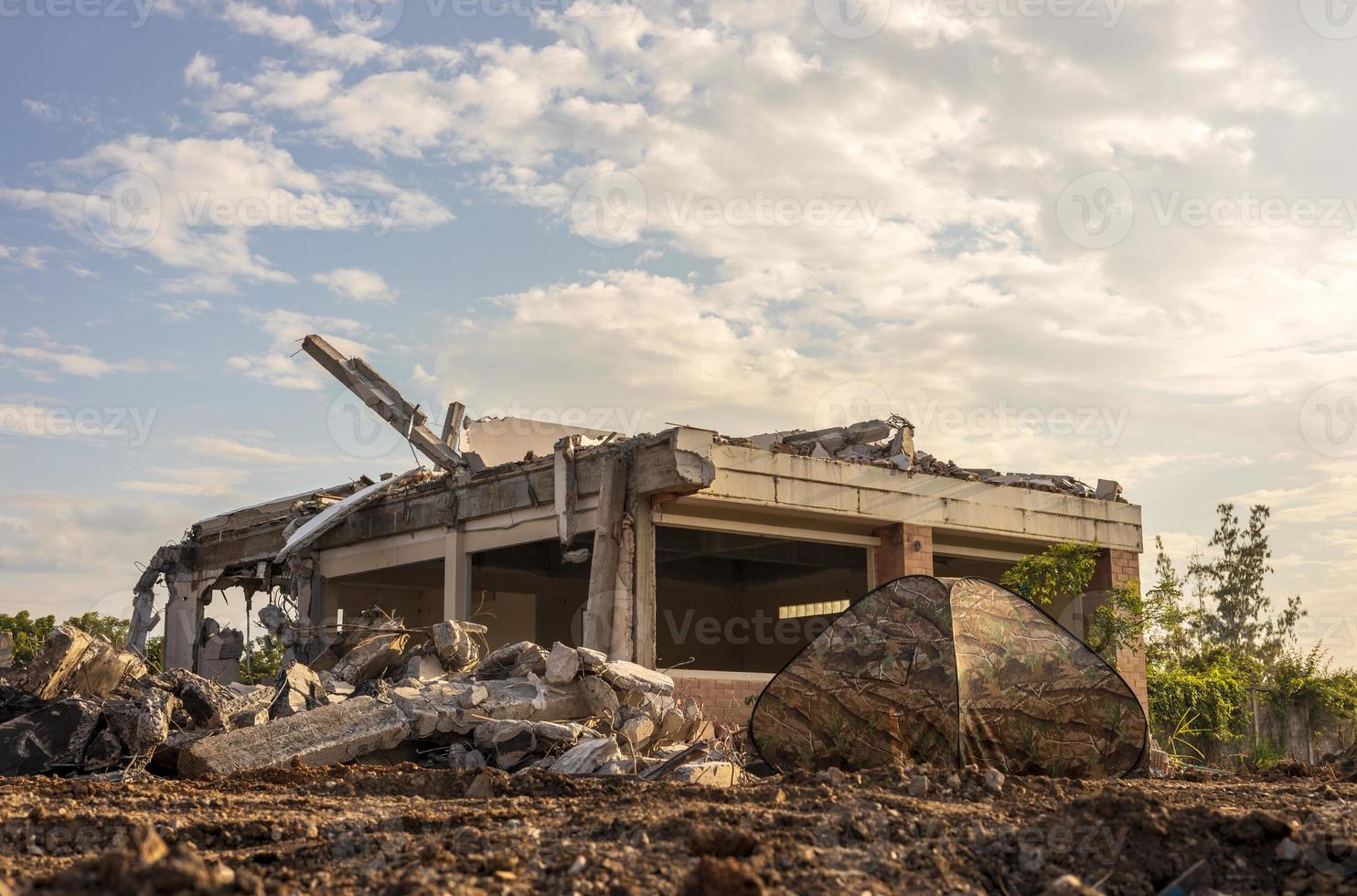 Low view of the ruins of a building with a military-patterned tent. photo