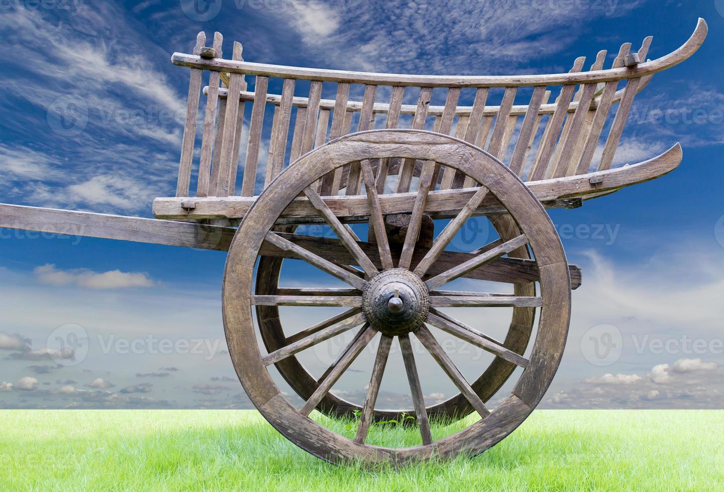 Side of an old wooden cart on grass with sky clouds. photo