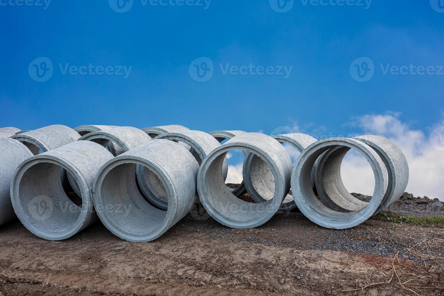 A low angle view of large concrete pipes lined up on the ground beside the road. photo