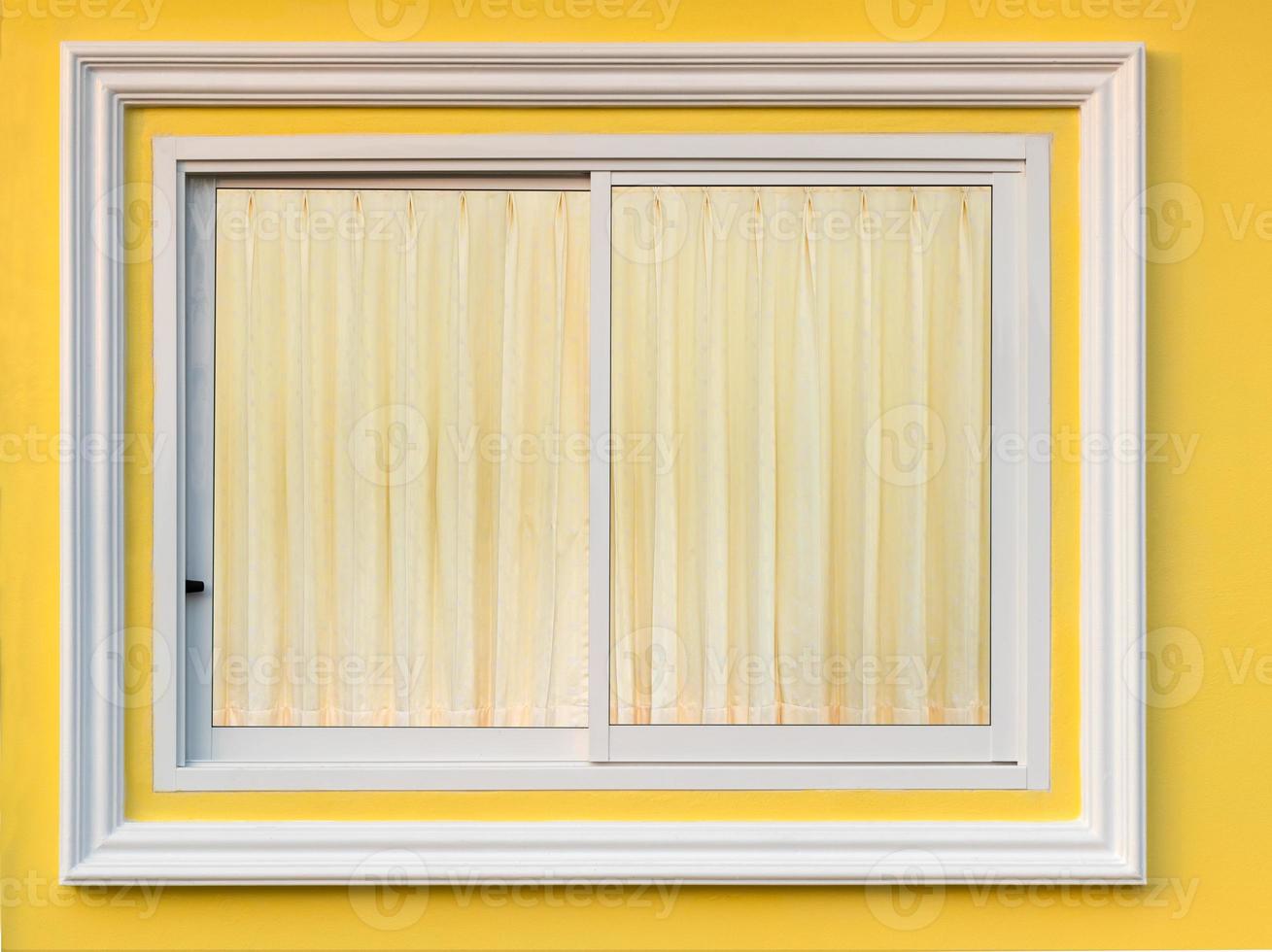 White frame window in yellow wall with curtain. photo