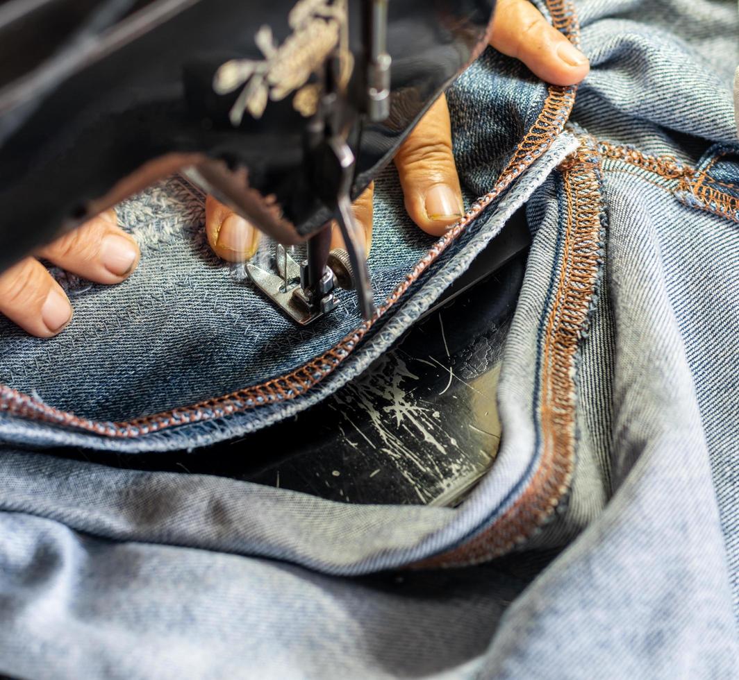 una mano cercana está reparando los jeans con una vieja máquina de coser. foto