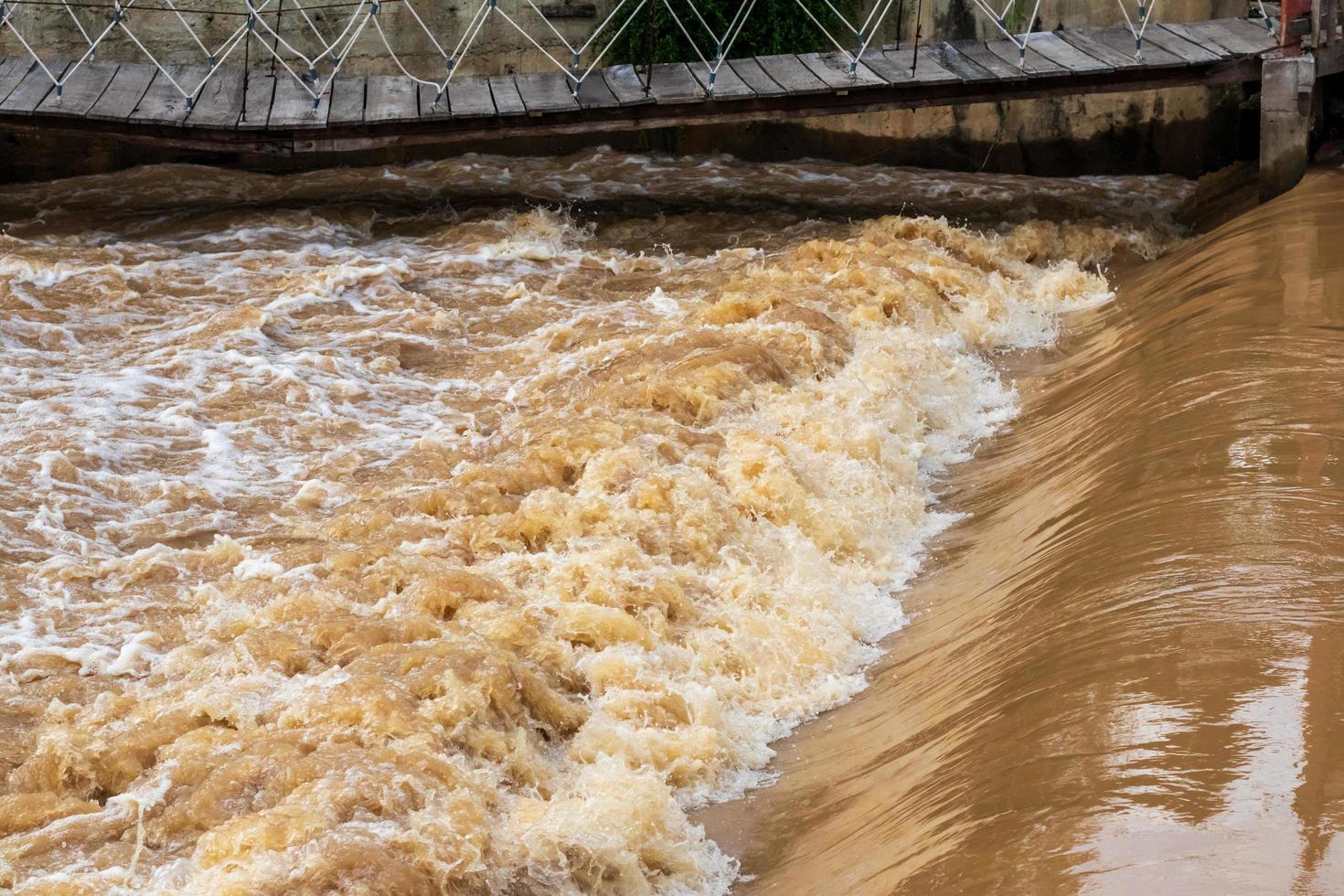 The turbid water rushed on the weir under the hanging bridge. photo