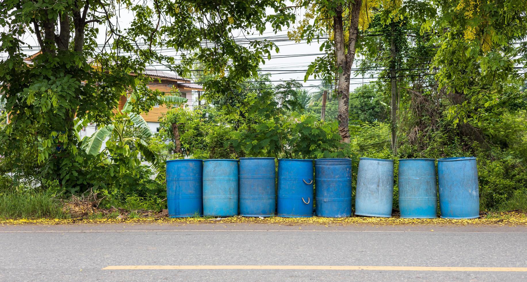 Old blue round plastic bins lined up on the side of the road. photo