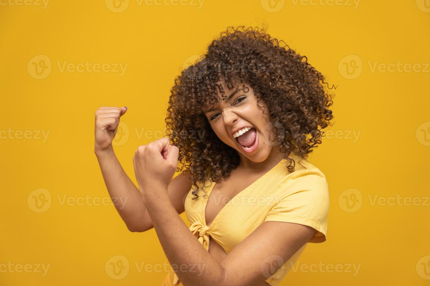 joven hermosa morena de cabello rizado felizmente regocijándose diciendo sí con fondo amarillo. concepto de éxito y logro. mujer bonita alegre sobre fondo amarillo. foto