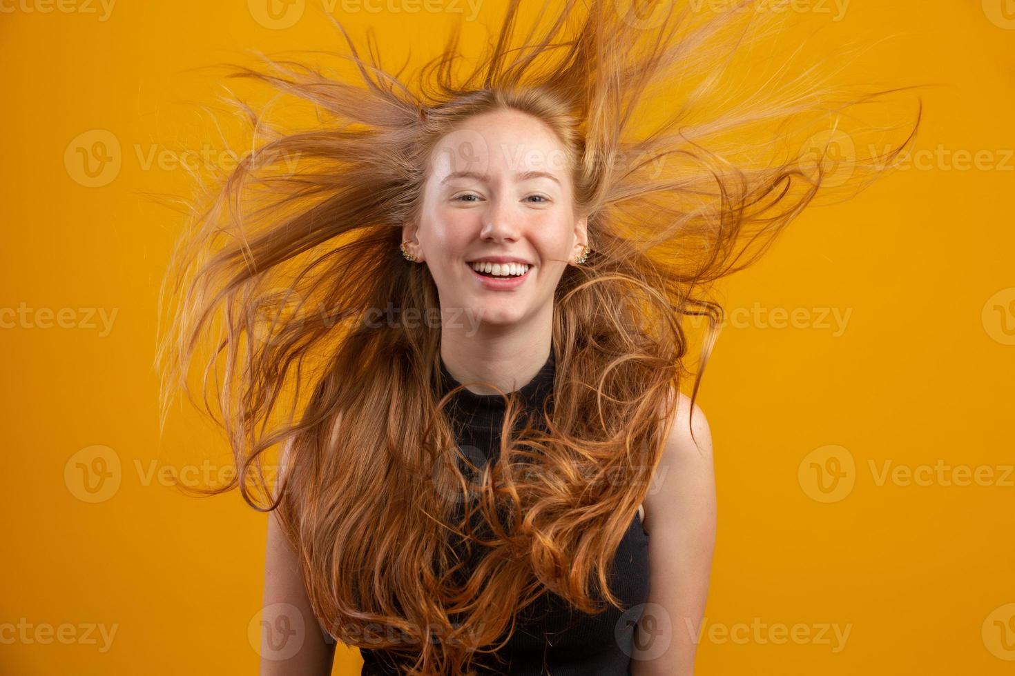 Portrait of beautiful cheerful redhead girl with flying hair smiling laughing looking at camera over yellow background. photo